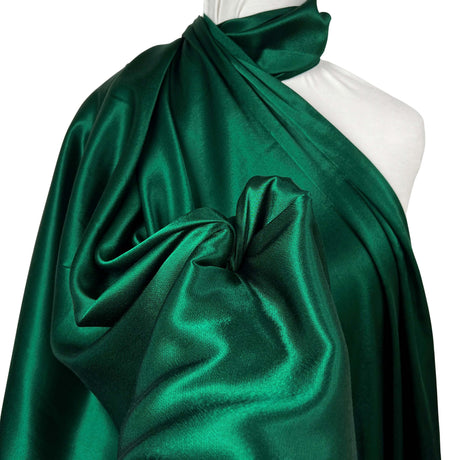 A dark emerald green satin fabric draped elegantly over a white mannequin torso, showcasing its smooth texture and reflective sheen against a clean white background.