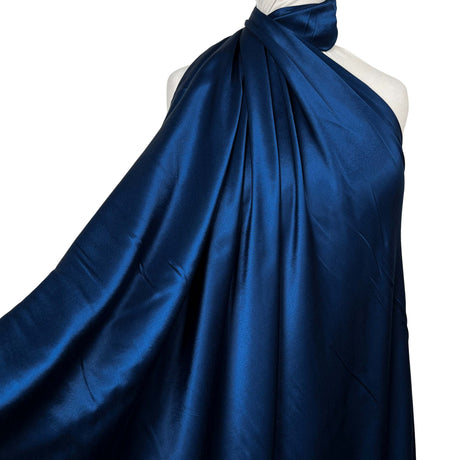 A deep blue satin fabric draped over a white mannequin torso against a plain white background.