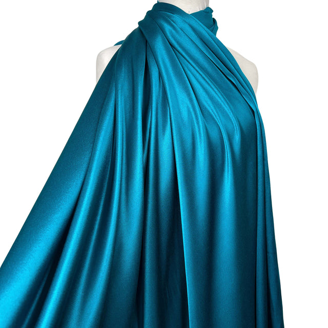A teal blue satin fabric draped elegantly over a white mannequin torso against a solid white background.