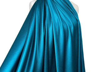 A teal blue satin fabric draped elegantly over a white mannequin torso against a solid white background.